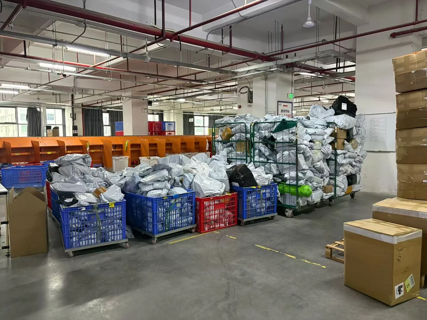 Overview of the warehouse sorting floor with crates of parcels, cage trolleys and a sorting machine in the background