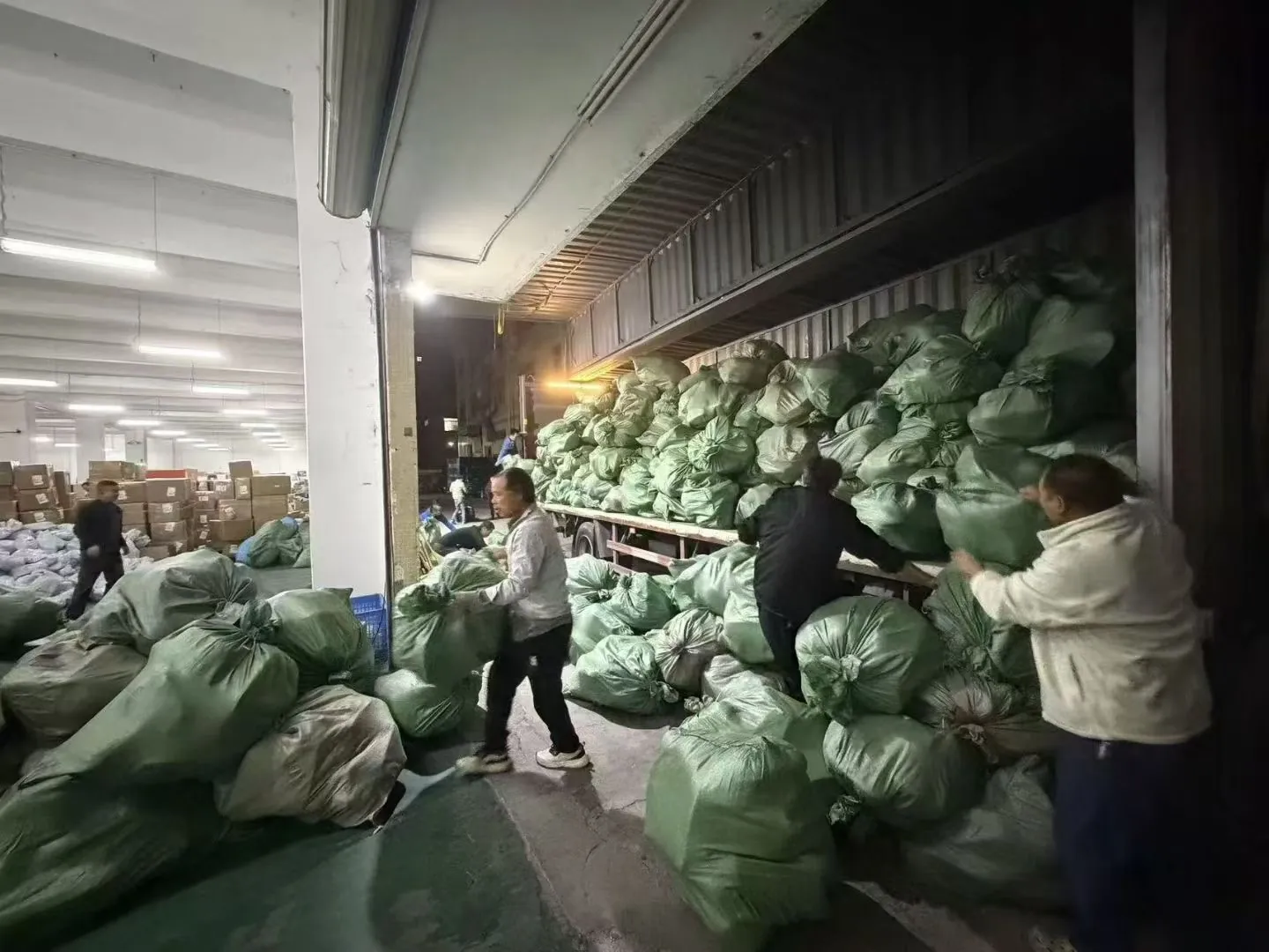 Warehouse workers moving large green sacks of parcels at the loading dock next to a truck